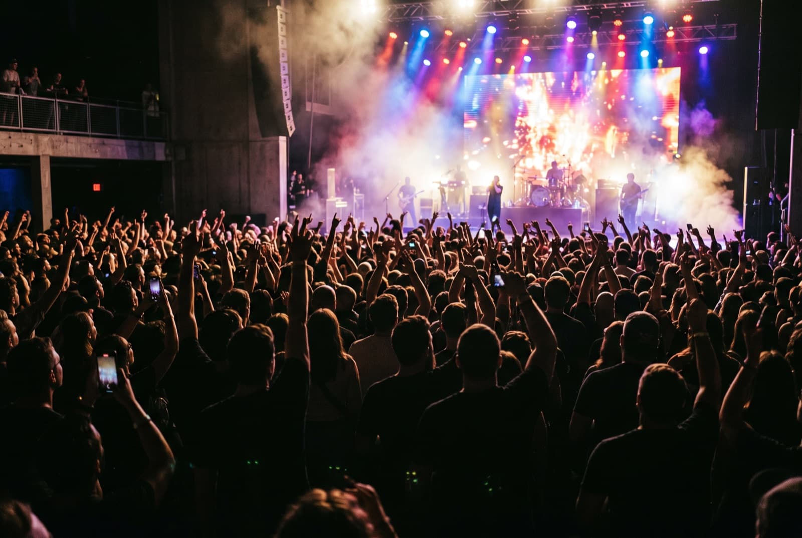 A packed concert crowd with hands raised toward a lit stage